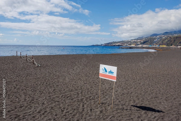 Fototapeta Empty beach with a coastal activity sign and calm sea under bright sky, capturing the stillness before summer begins.