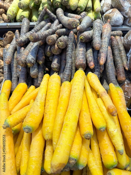 Fototapeta Assorted fresh vegetables on display at a local market, including black carrots, yellow carrots and green carrots. Colorful and neatly arranged root vegetables for sale