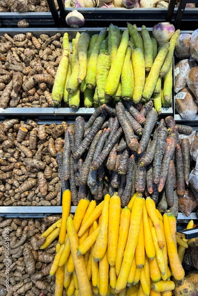 Fototapeta Assorted fresh vegetables on display at a local market, including turmeric, black carrots, yellow carrots and green carrots. Colorful and neatly arranged root vegetables for sale