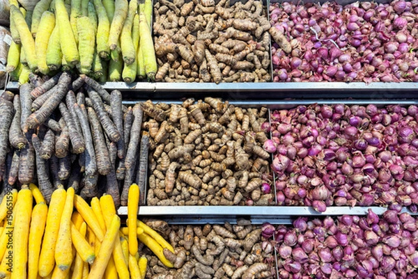 Fototapeta Assorted fresh vegetables on display at a local market, including turmeric, shallots, black carrots, yellow carrots and green carrots. Colorful and neatly arranged root vegetables for sale