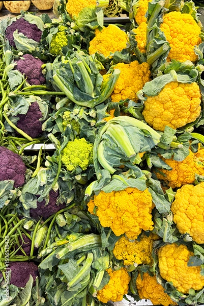Fototapeta Fresh purple, yellow, and green cauliflower heads displayed at a local market. Colorful and healthy vegetables neatly arranged for sale. Organic produce.