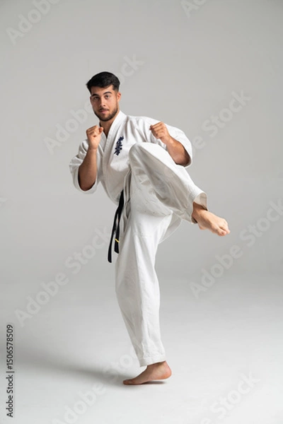 Fototapeta Kyokushinkai karate fighter kicking high in studio setting