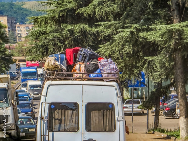 Obraz A van, packed high with luggage, including a bewildered-looking sheep, navigates a bustling street in Kutaisi, Georgia.