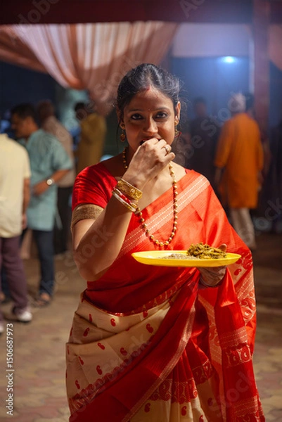 Obraz Traditional Bengali Woman Enjoying Bhog During Kali Puja Celebration in Red Saree