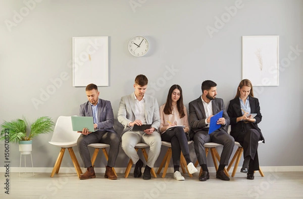 Fototapeta Young hr applicants sitting in queue preparing for important interview in office, vacancy candidates waiting on chairs holding resume, human resources, people hiring and job search, worried before