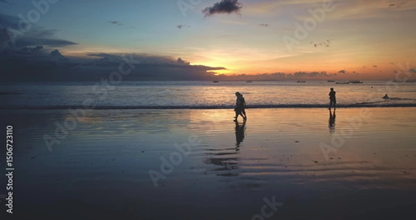 Obraz Tourists walking along Dreamland Beach in Bali, Indonesia, during a vibrant sunset, soaking in the stunning scenery and tranquil ocean waves, creating a perfect evening atmosphere