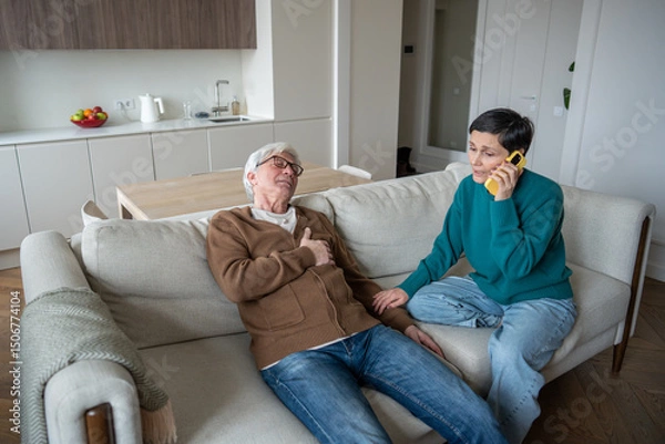 Fototapeta Concerned wife makes urgent call during husband heart attack. Senior male collapsing, chest pain, panic in room, aging health risk, cardiovascular failure, immediate assistance and domestic emergency