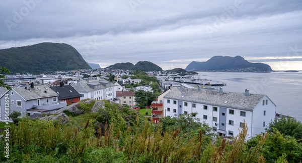 Fototapeta Scenic view of a residential neighborhood in Alesund, Norway, seen from Mount Aksla, with white houses, a coastal bridge, and mountainous islands in the background.