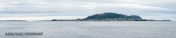 Fototapeta Cloudy day over Giske island near Ålesund, Norway, featuring green meadows, calm sea, and rugged coastline under a soft, diffused light on the western fjords
