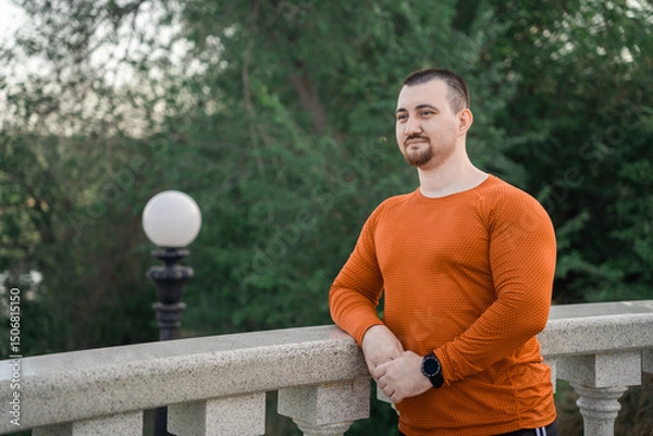 Fototapeta A man in workout clothes rests on a railing with a scenic view