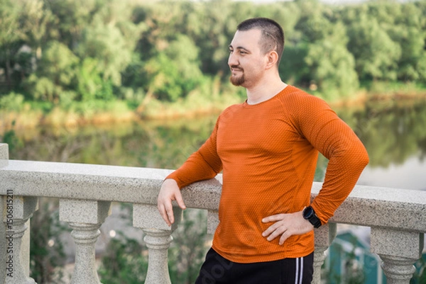 Fototapeta A man in workout clothes rests on a railing with a scenic view