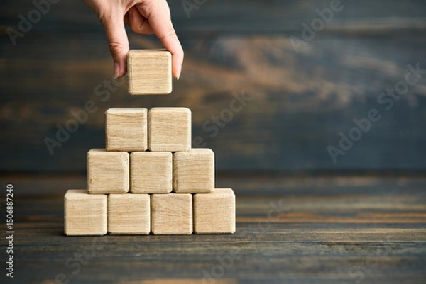 Fototapeta Hand placing last wooden cube on pyramid stack
