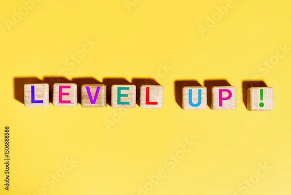 Fototapeta Colorful "Level Up" text  on wooden blocks over bright yellow background