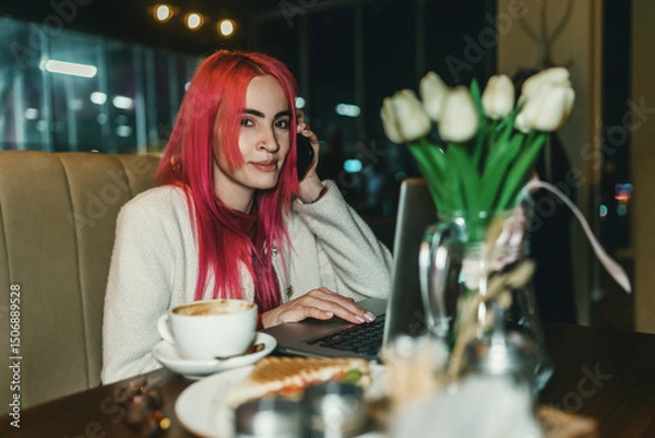 Fototapeta A woman with red hair is sitting with a laptop in a cafe