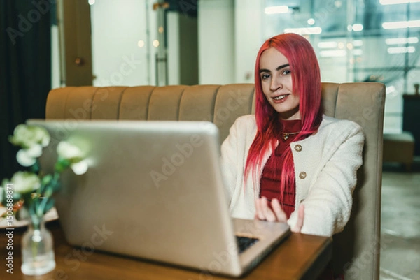 Fototapeta A woman with red hair is sitting with a laptop in a cafe