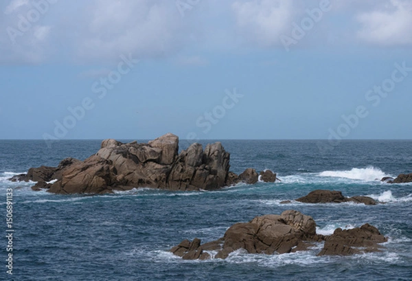 Obraz View from the Galician coast towards the Atlantic Ocean of the waves breaking against a scattered structure of rocks and foam and the blue sky with clouds separated from the water by the horizon