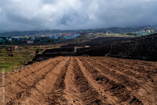 Obraz A field of dirt with a cloudy sky in the background. The sky is overcast and the field is empty