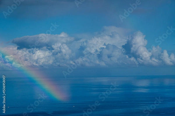 Obraz A rainbow is seen in the sky above the ocean. The sky is dark and cloudy, and the water is calm