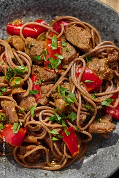 Fototapeta Wok with Soba noodles with turkey, mushrooms and sweet red bell pepper in plate on wooden table in the sun. Asian food, concept of street food. Top view. Close up.
