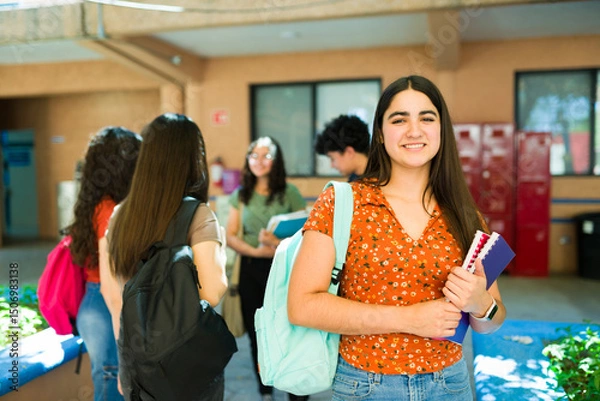 Obraz Smiling high school student carrying backpack and books on campus