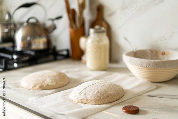 Obraz Freshly prepared sourdough bread dough rests on parchment near a container of active starter and a mixing bowl, showcasing the art of home baking.