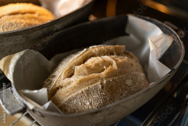 Obraz Two golden-brown loaves of bread rest in baking containers inside an oven, their crusts glistening with warmth as they await to be served. The inviting aroma fills the air.