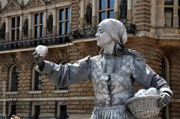 Obraz Die stillstehende Marktfrau auf dem Hamburger Marktplatz. Die Straßenkunst der Straßenkünstlerin als lebende Statue. Sie bietet Äpfel zum Kauf an,  Gesundheit.