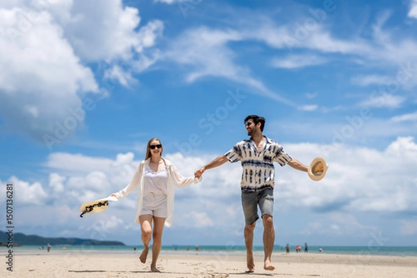 Obraz Couple walks hand in hand along sandy beach under bright clouds on sunny day