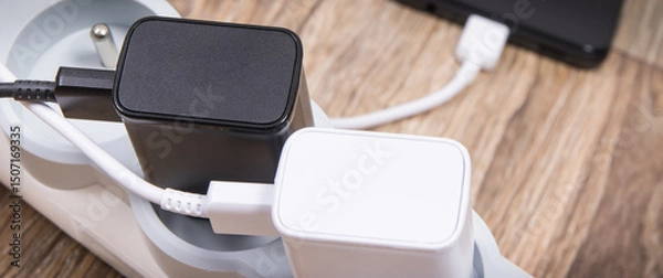 Obraz Black smartphone and chargers connected to electrical power strip. Various devices charging concept
