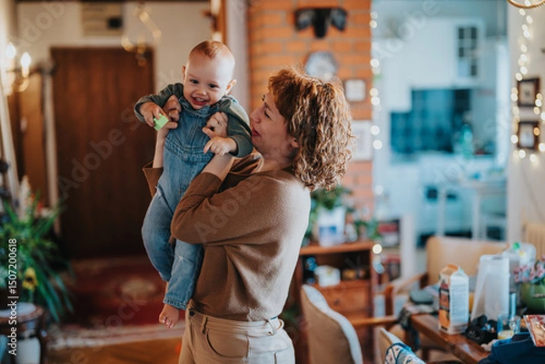 Fototapeta A happy parent lifts and plays with their infant at home, creating joyful bonding moments amidst a cozy and vibrant domestic setting.