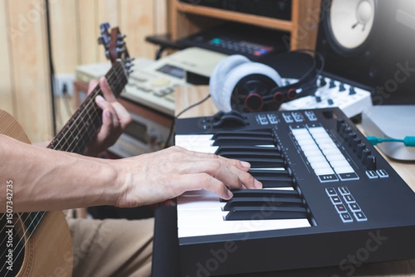 Obraz close up male musician hand playing midi keyboard and acoustic guitar for composing a song. song writing, music production concept