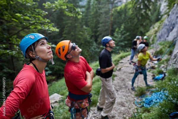 Fototapeta Climbers prepare for an ascent while studying a rock face in a forested area