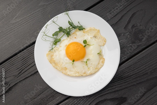 Obraz A sunny side up egg with fresh micro greens on a white plate over dark wood.