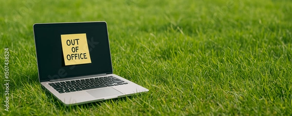 Fototapeta Open laptop on a grassy field with bold OUT OF OFFICE message on screen. Concept of digital detox, outdoor work break, or vacation mode in nature