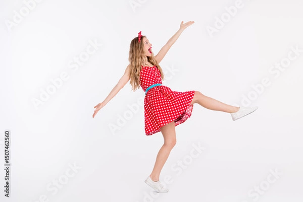 Fototapeta Young woman in a retro polka dot dress dancing joyfully against a white background, stylishly showcasing vintage charm and cheerful energy