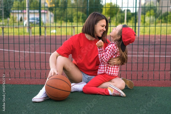 Obraz Funny laughing mom and daughter relax on the playground after playing basketball