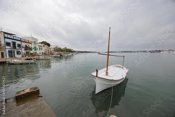 Fototapeta White llaüt moored in portocolom, mallorca, spain, reflecting on the calm water of the port