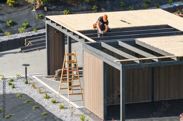 Fototapeta Construction Worker Installing Wooden Beams on a Modern Building Structure in a Suburban Area