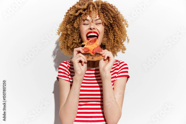 Obraz Happy young woman enjoying pizza with red sauce, wearing a striped shirt on a white background, showcasing joy and delicious food cravings
