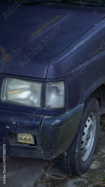 Obraz Close-up of a weathered dark-colored minivan's front end, showing signs of age and wear.