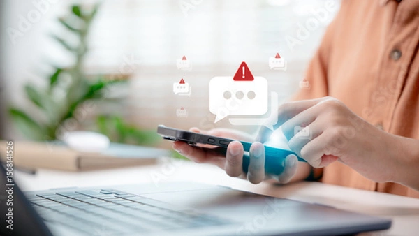 Obraz Close-up hand holding smartphone with spam alert icon popping up, concept of online scam warning, phishing message, cybersecurity, and mobile security notification.