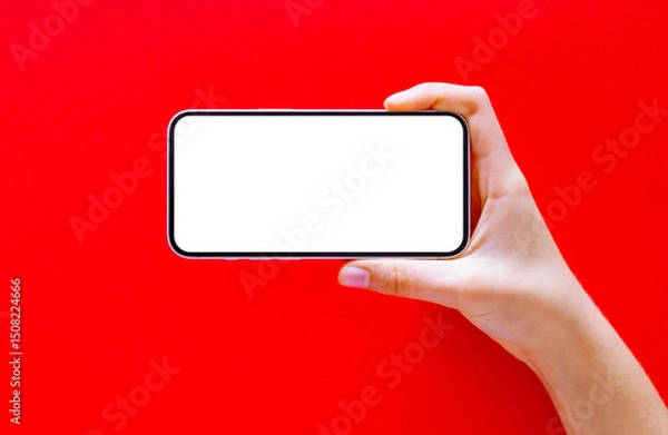 Fototapeta Mobile phone horizontally in hand on red background