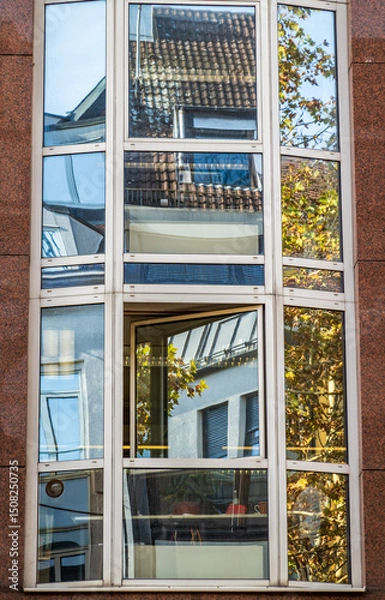Obraz Modern glass facade reflects neighboring buildings in urban setting during daylight hours