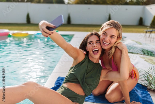 Fototapeta Two beautiful girls taking photo of themselves by the poolside