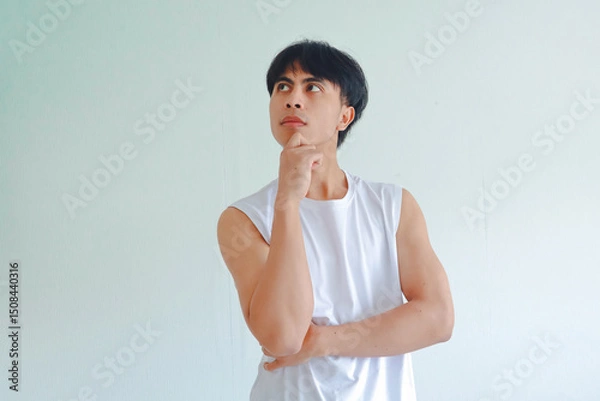 Fototapeta Portrait of a young Asian man from Southeast Asia with hand on chin in thoughtful pose, isolated on white background, representing thinking and contemplation