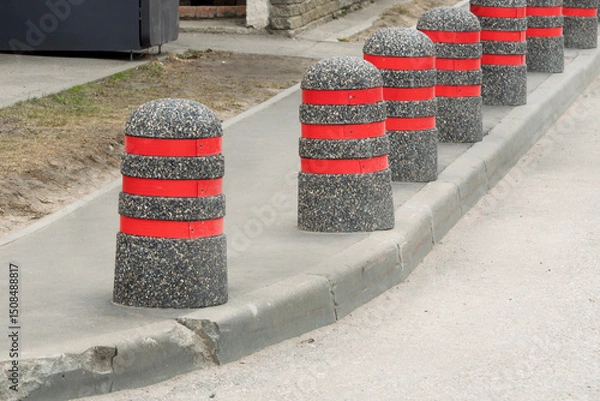 Fototapeta Concrete bollards with bright red stripes line urban sidewalk, creating visual rhythm and enhancing pedestrian safety in cityscape.