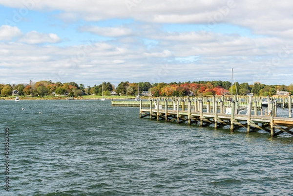 Fototapeta Empty wooden piers in a harbour on a partly cloudy autumn day. Anchored boats are visible in background.