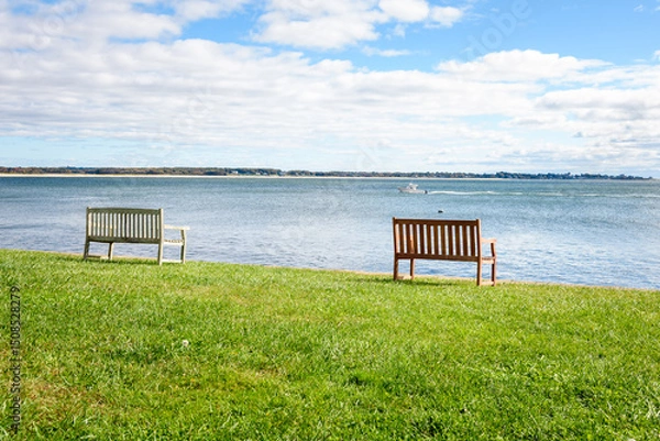 Fototapeta Empty wooden benches on grass facing a bay along the coast of Connecticut on a sunny autumn morning