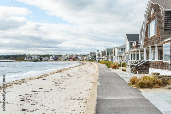 Fototapeta Empty paved footpath lined with tradtional wooden houses along a sandy beach on a cloudy autumn day