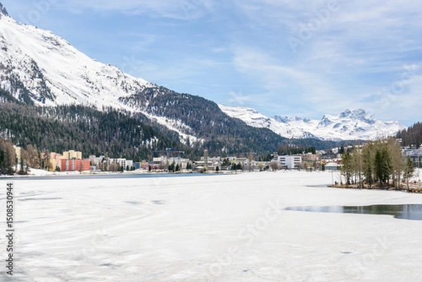 Fototapeta Apartment buildings on the shore of frozen lake St. Moritz on an early spring day. Canton of Grisons, Switzerland.